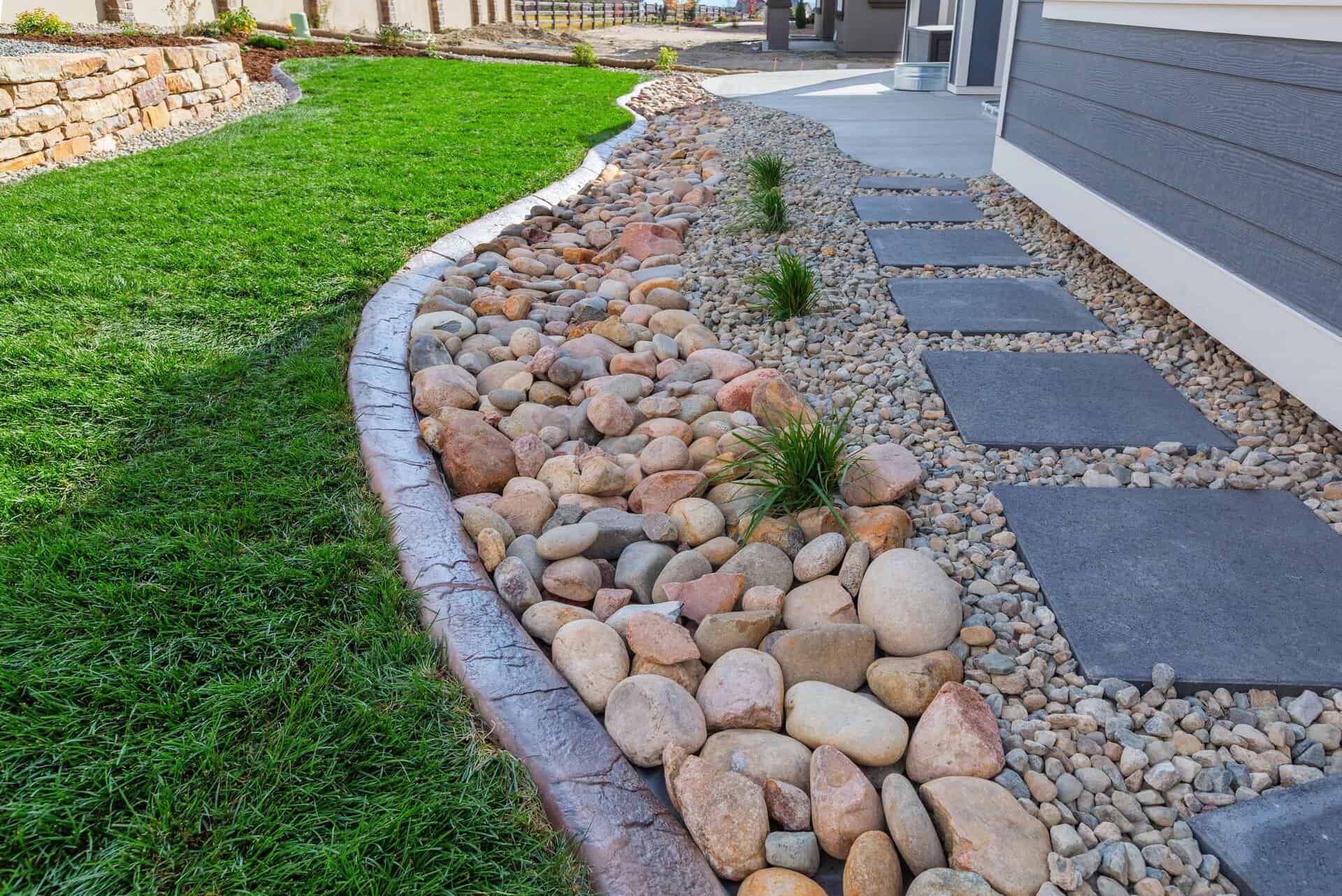 A landscaper-designed yard features a dry riverbed of large river rocks, bordered by grass and a stone path leading to the house.